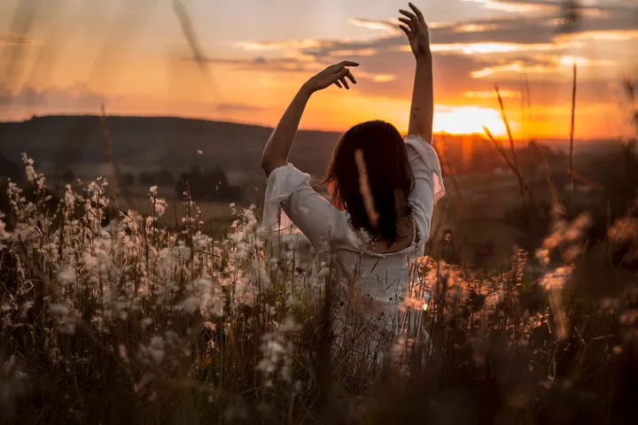 Persona d'esquena aixecant els braços lentament a la posta de sol